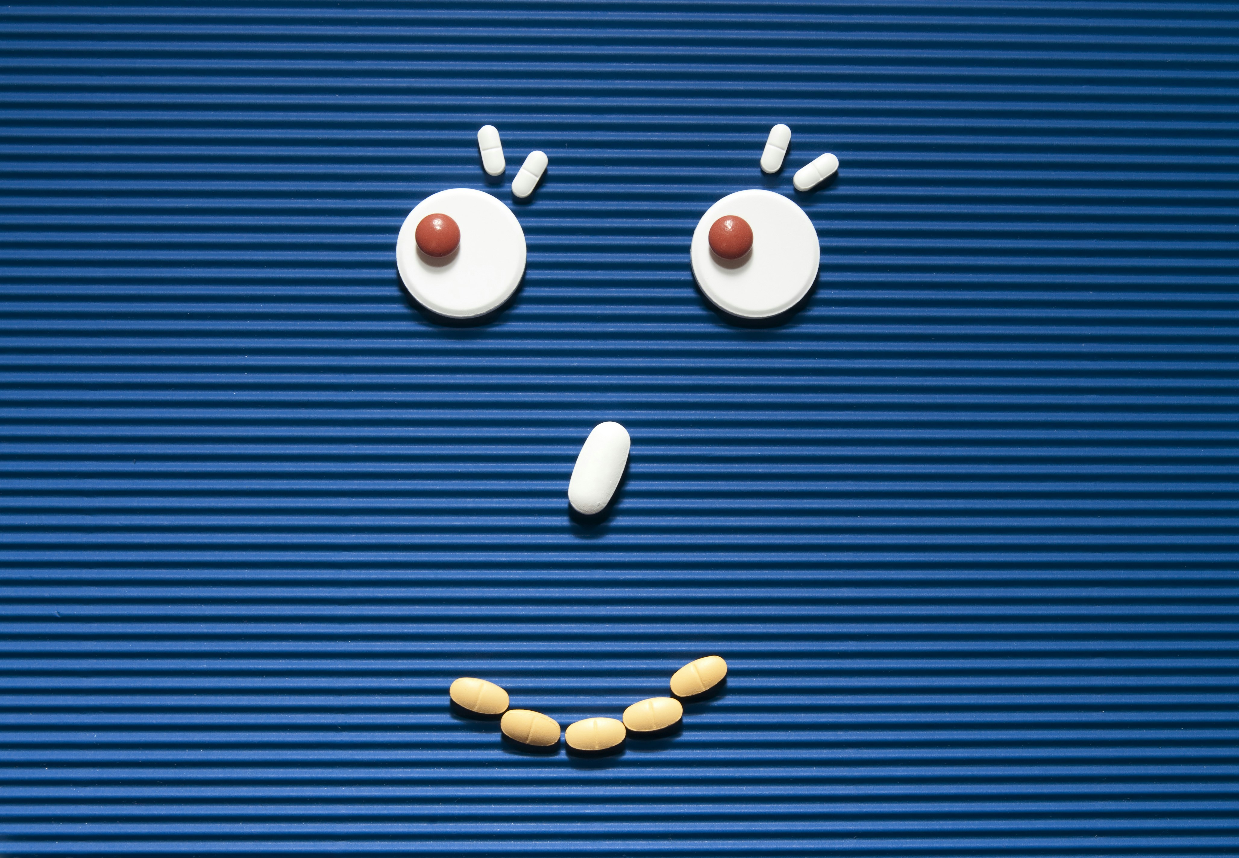 Prescription pills arranged on a blue surface in the shape of a happy, smiling face.